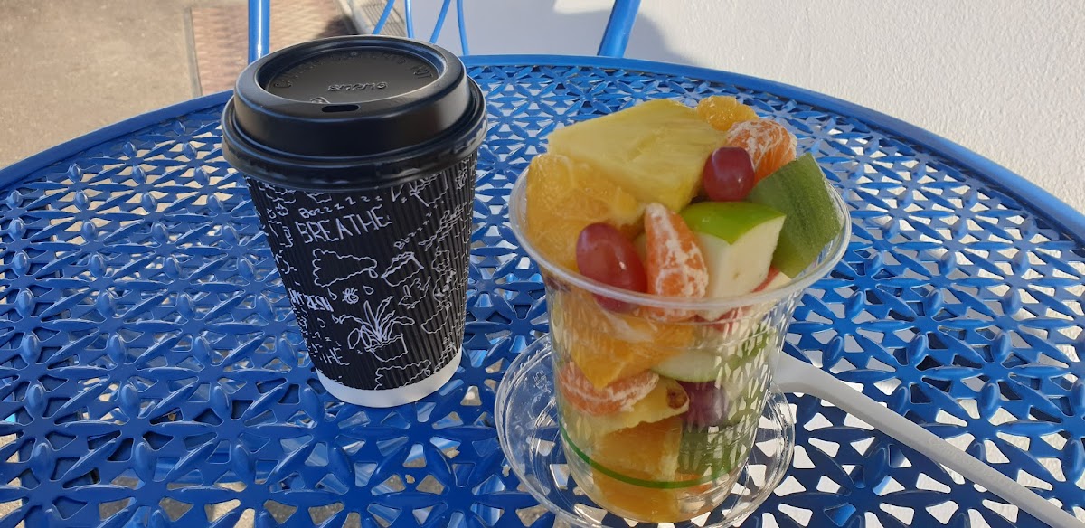 Fresh coffee and a fruit salad cup on a sunny table at Make n Bake